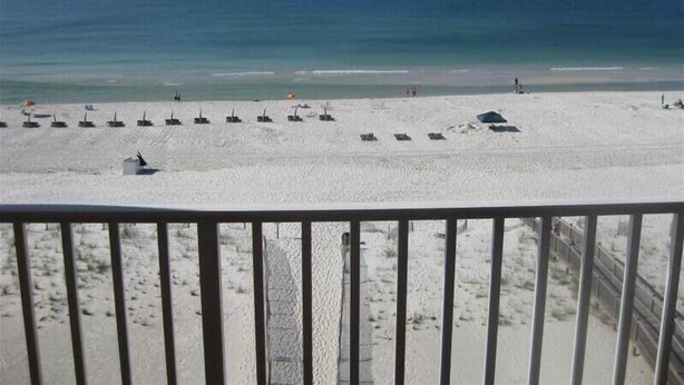 Una spiaggia con file di lettini e ombrelloni, una vista chiara sull'oceano e una ringhiera in primo piano.