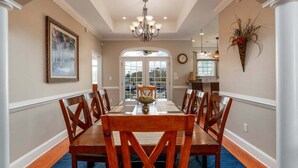 A dining room with a long wooden table and chairs, a chandelier, and a large window with a view. - Condo pool garage short walk to beach (Myrtle Beach)