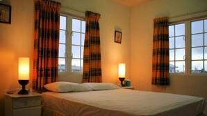 Una habitación de hotel con una cama, dos lámparas de noche, una mesita de noche y una ventana con cortinas.