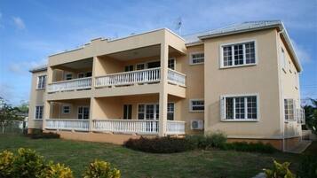 Stylish two-story building with a central balcony and two upper-floor balconies, surrounded by a lush garden.