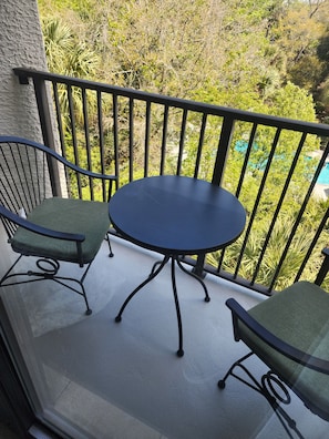 Balcón con una mesa redonda y dos sillas, rodeado de baranda, con vista a una piscina y abundante vegetación.