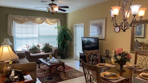 Una sala de estar con sofá, mesa de centro, televisor, candelabro, mesa de comedor y sillas.
