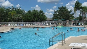 Una piscina con varias pistas, rodeada de sillones de descanso y palmeras.