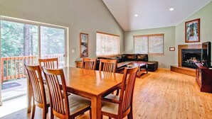 A spacious living room with a wooden dining table and chairs, a fireplace, and large windows offering a view of the outdoors. - Sequoias East (Yosemite National Park)