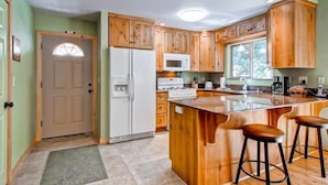 A kitchen with wooden cabinets, a white refrigerator, a microwave, a sink, and a large island with stools. - Sequoias East (Yosemite National Park)