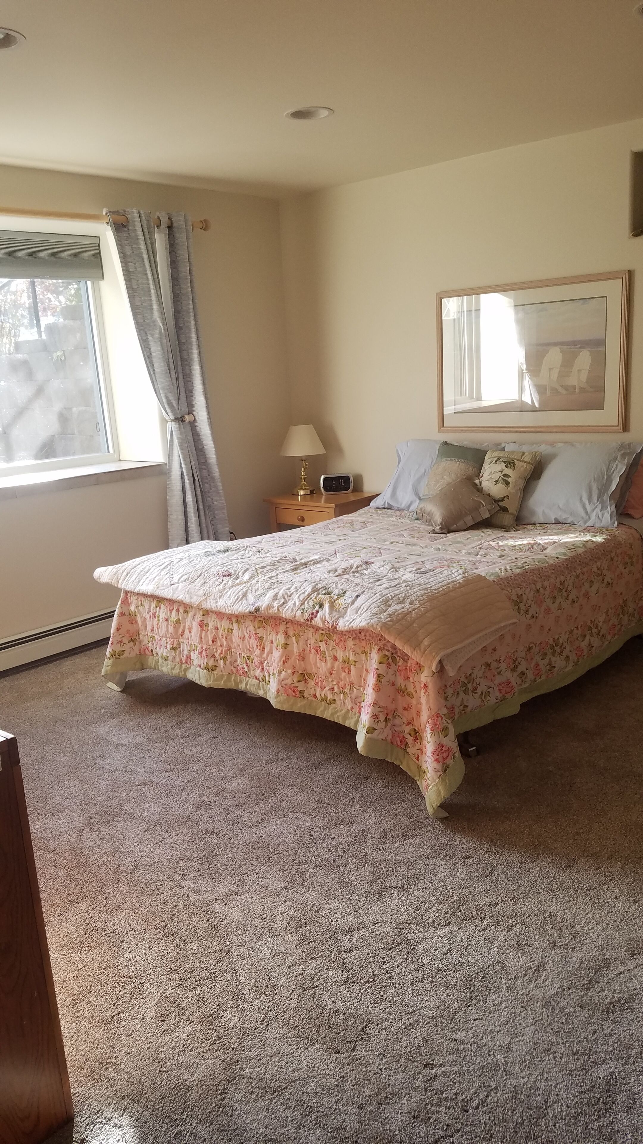 A bedroom with a bed, a nightstand, a lamp, a framed picture on the wall, and a window with curtains.