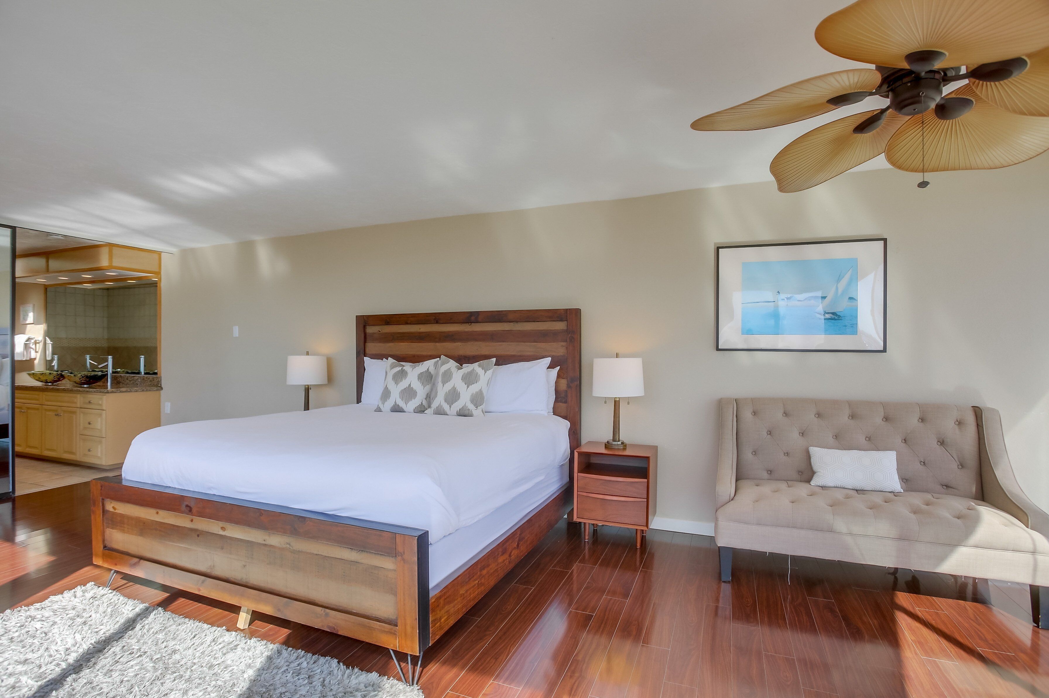 A bedroom with a wooden bed, a nightstand, a beige sofa, a ceiling fan, and a framed picture on the wall.