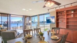 Uma sala de jantar com vista para o mar, um ventilador de teto e uma televisão na parede.