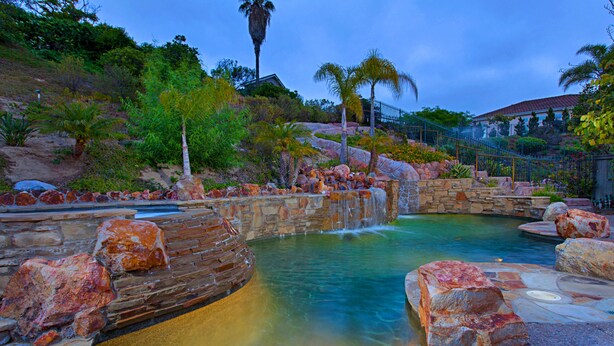 Un área de piscina con formaciones rocosas naturales y una cascada.