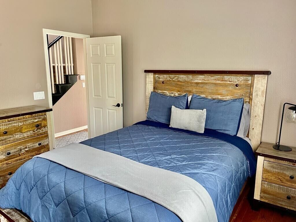 A bedroom with a bed, a wooden headboard, a nightstand, a dresser, and a door leading to a staircase.