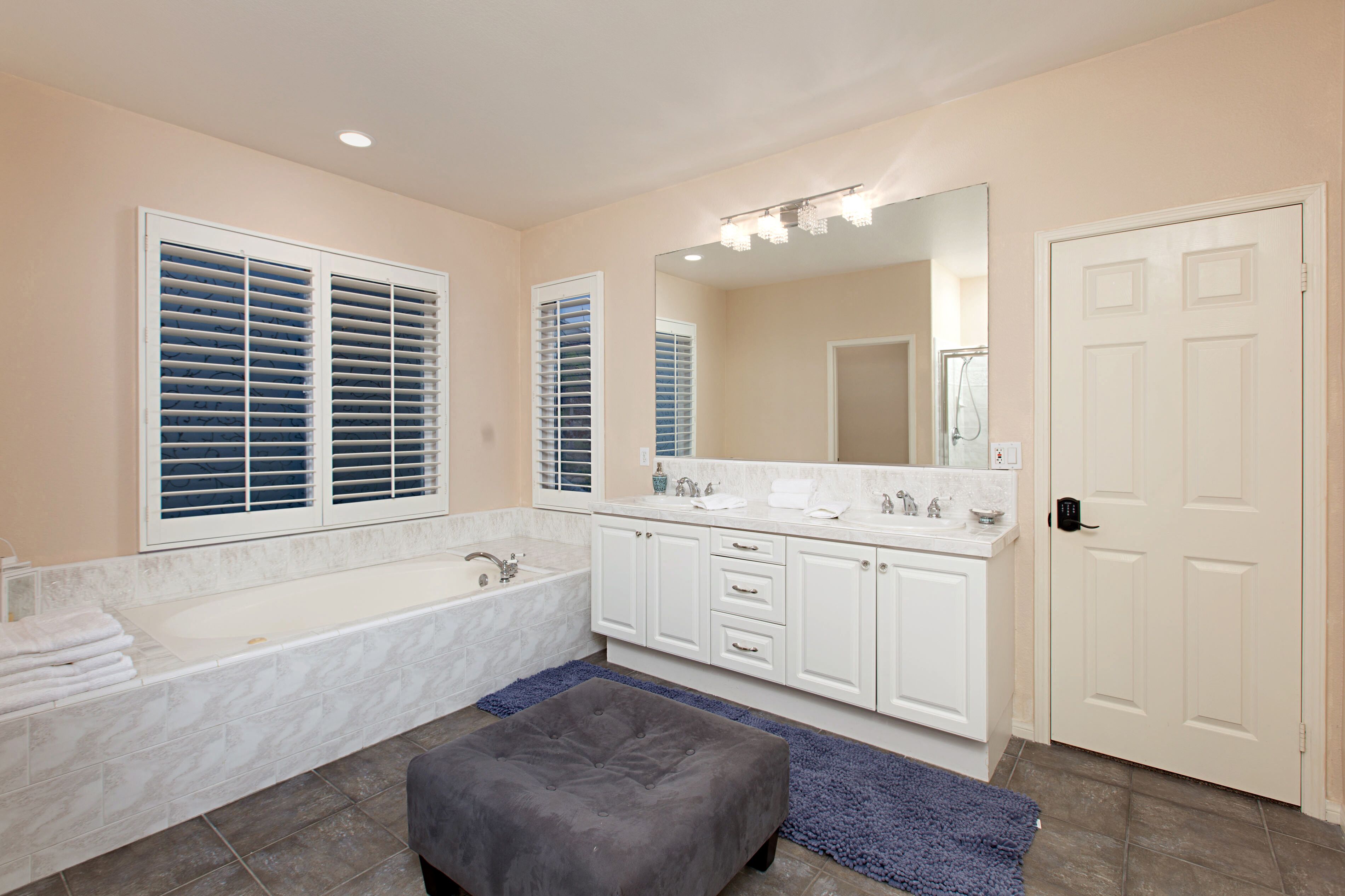 A bathroom with a large bathtub, a double vanity with a mirror, and a door.