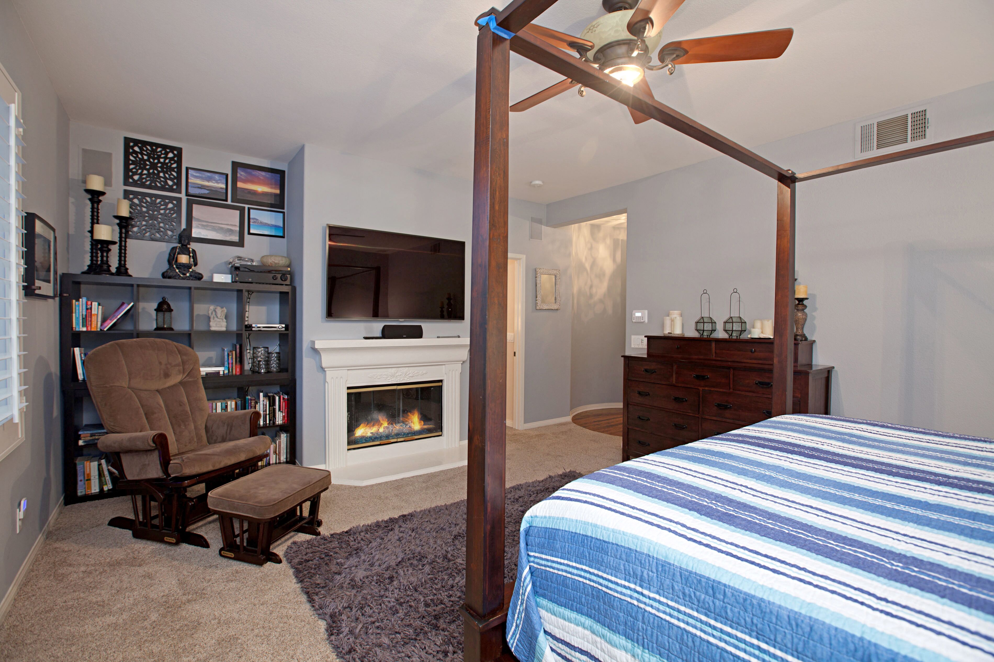 A bedroom with a four-poster bed, a fireplace, a bookshelf, and a television.