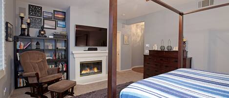 A bedroom with a four-poster bed, a fireplace, a bookshelf, and a television.