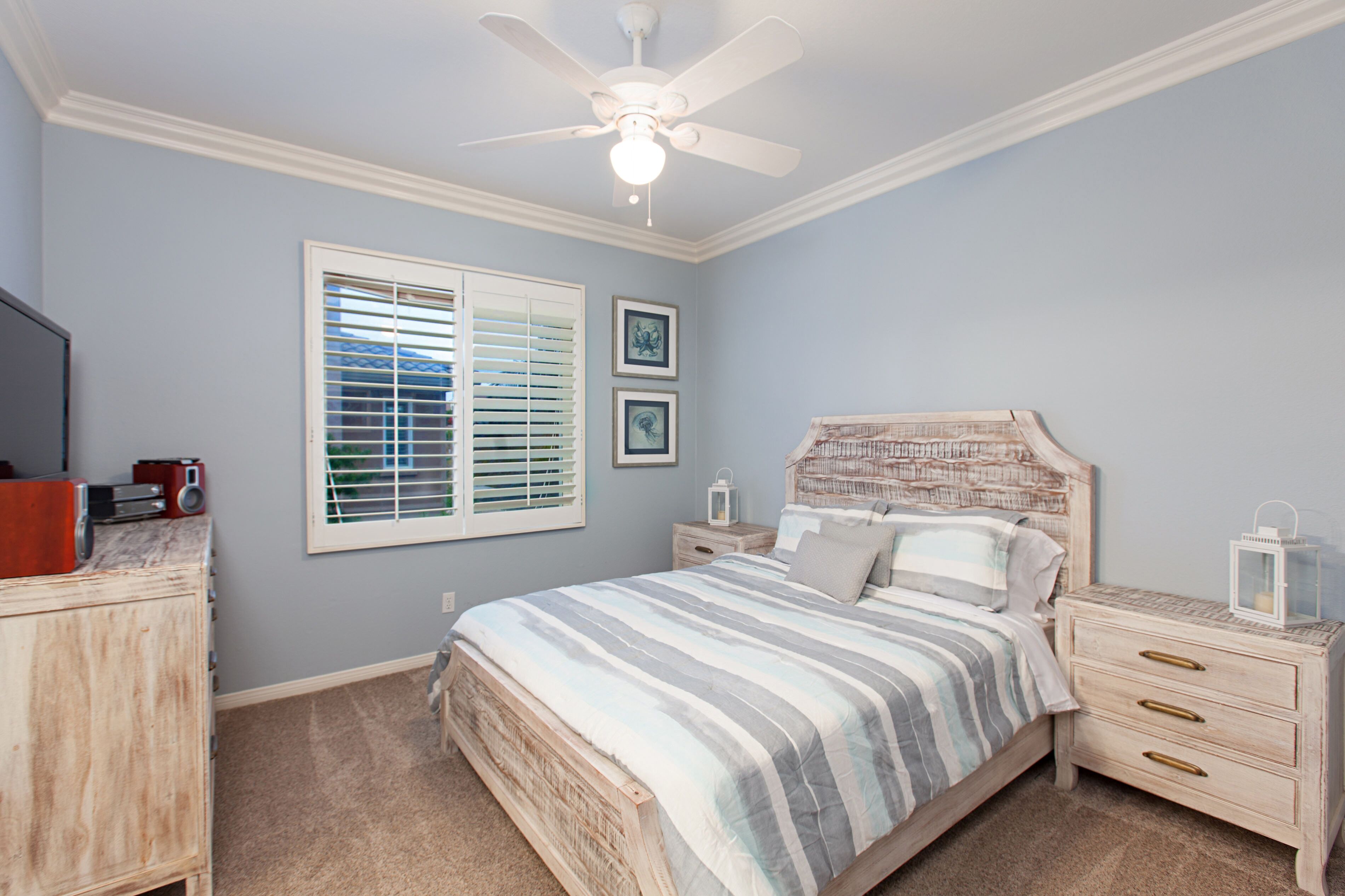 A bedroom with a bed, a nightstand, a dresser, a ceiling fan, and a window with blinds.