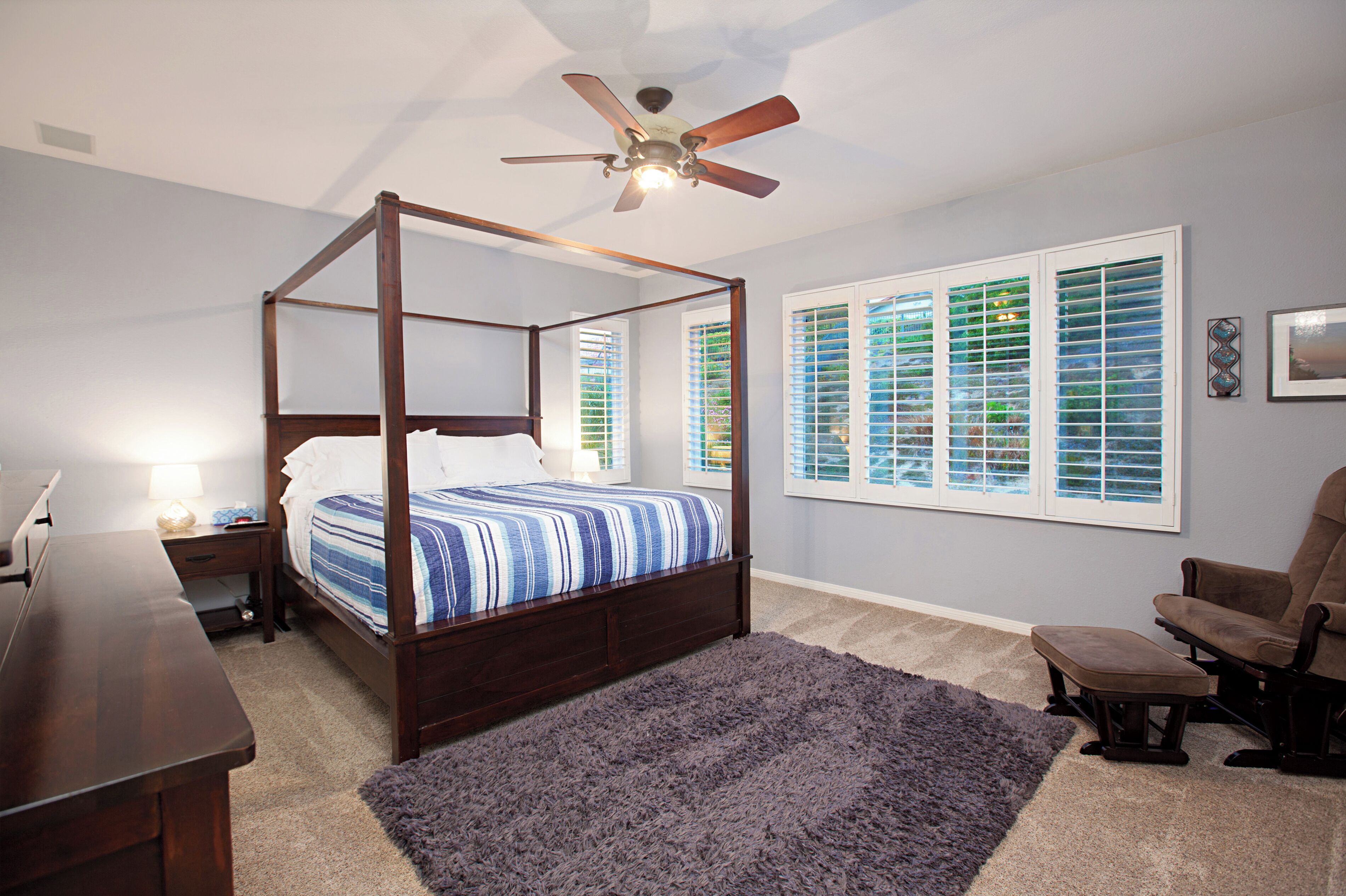 A four-poster bed with a dark wooden frame, a blue and white striped bedspread, and a ceiling fan above.