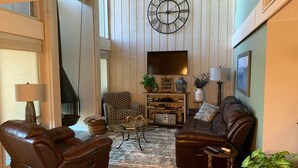 A living room with leather sofas, a patterned armchair, a glass coffee table, a clock on the wall, and a fireplace. - Lake Travis Retreat - Water View (Leander)