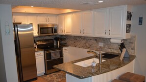 A kitchen with white cabinets, stainless steel appliances, a granite countertop, and a small island with stools. - Lake Travis Retreat - Water View (Leander)