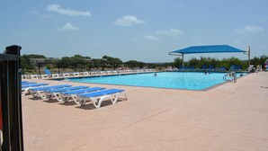 A swimming pool with blue and white lounge chairs, a shaded area, and a clear sky. - Lake Travis Retreat - Water View (Leander)