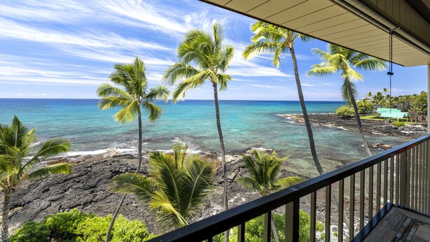 Een balkon met uitzicht op een tropisch strand, palmbomen en een helderblauwe zee.