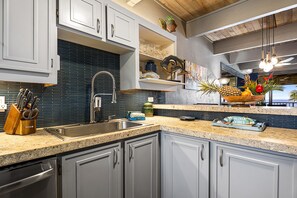 A kitchen with a granite countertop, stainless steel sink, and white cabinets.