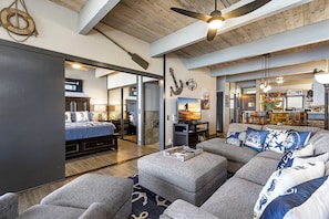 A spacious living area with a large grey sectional sofa, a flat-screen TV, and a ceiling fan.