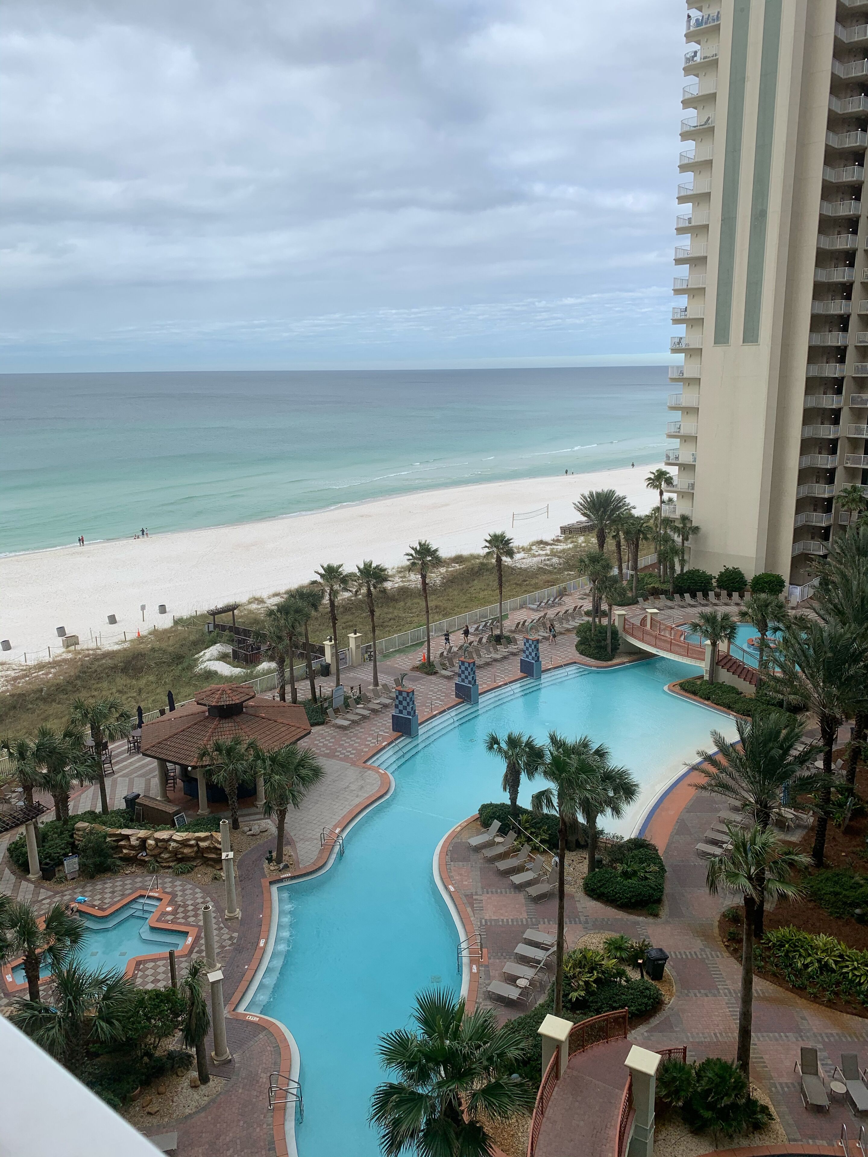 A resort with a large swimming pool, a beach, and a tall building.
