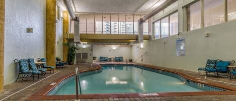 Une piscine intérieure avec un sol en briques, des chaises bleues à motifs et un panneau indiquant les règles à respecter dans la piscine intérieure.
