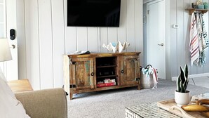 Un salon avec un plafond en bois, un téléviseur fixé au mur, un meuble en bois et une table basse à motifs.
