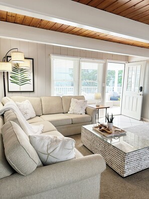 Ein Wohnzimmer mit einem beigefarbenen Ecksofa, einem Glastisch und einer gerahmten Pflanze.