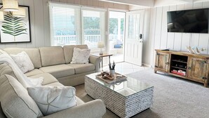 Un salon avec un canapé beige, une table basse en verre, un meuble en bois et un téléviseur fixé au mur.