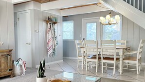 Un vaste salon doté d’un haut plafond, un coin repas avec des meubles blancs et un escalier menant à l’étage supérieur.