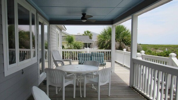 A covered outdoor deck with a table and chairs, a white railing, and a view of the ocean. - 709 Bluefish - Ocean Front (Saint Helena Island)