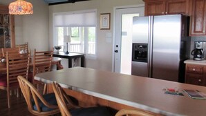 A kitchen with a stainless steel refrigerator, wooden chairs, and a long dining table. - 709 Bluefish - Ocean Front (Saint Helena Island)