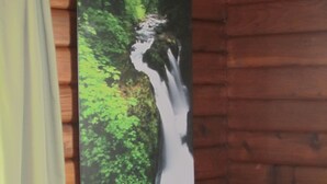 A room with wooden walls, a bed with a striped bedspread, and a framed picture of a waterfall.