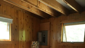 A wooden cabin bedroom with a bed, a nightstand, a lamp, and a window.