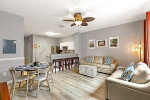 A modern living room with a dining area, a kitchen, and a ceiling fan.
