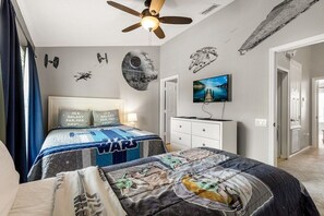 A bedroom with a bed, a ceiling fan, a TV, and Star Wars-themed decorations.