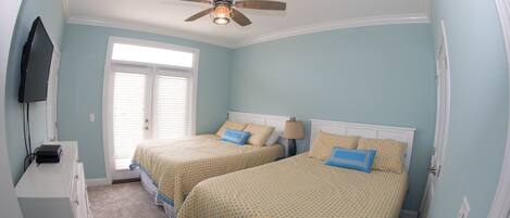 A bedroom with two beds, a ceiling fan, a TV mounted on the wall, and a window with blinds.