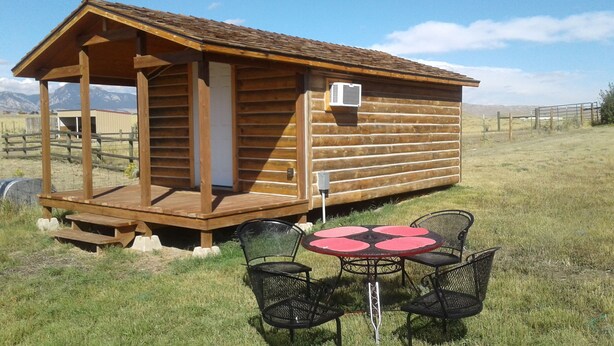 Una cabaña de madera con un porche y una pequeña mesa con sillas.