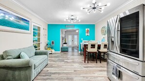 A modern kitchen with a large refrigerator, a dining area with a table and chairs, and a teal-colored wall with a 'Beach House' sign. - Longboat Key bliss. A perfect Retreat at Cabana Beach Club #9.Also available#8  (Longboat Key)