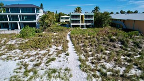 A coastal property with a sandy beach, a clear path leading to a building with multiple balconies, and a backdrop of palm trees. - Longboat Key bliss. A perfect Retreat at Cabana Beach Club #9.Also available#8  (Longboat Key)