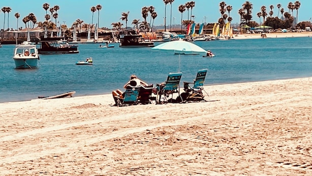 Una playa con una hilera de palmeras, un bote y una fila de sillas de playa.