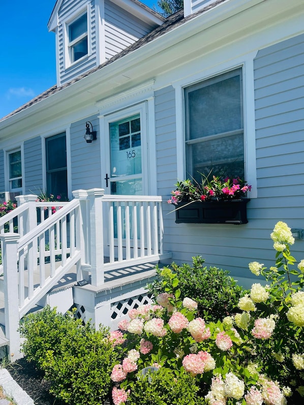 A two-story house with a white exterior, a front porch with a white railing, and a mailbox with the number 165.