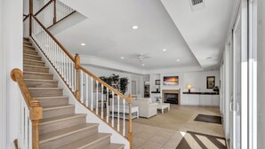 A spacious living area with a wooden staircase, a fireplace, and a kitchen area. - Ocean View, 3-Patio, 6BR, 6300sf Home w/Pool; 50 Steps to Beach, Coligny Circle! (Hilton Head Isalnd)