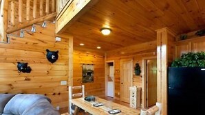 A wooden cabin interior with a dining area, a sofa, and a staircase. - A Bear's Kind of Fun in Pigeon Forge #unforgettable 4 bedroom w/ Games & Full Theater! (Sevierville)