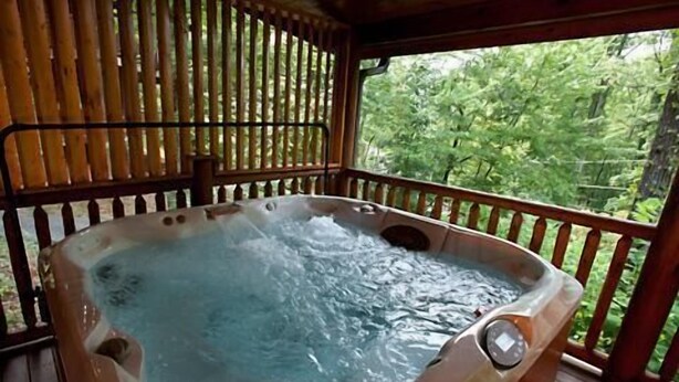 A hot tub with a wooden deck and a view of greenery. - A Bear's Kind of Fun in Pigeon Forge #unforgettable 4 bedroom w/ Games & Full Theater! (Sevierville)