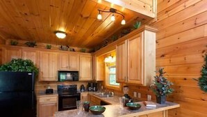 A wooden cabin kitchen with a central island, wooden cabinets, a black refrigerator, and a microwave. - A Bear's Kind of Fun in Pigeon Forge #unforgettable 4 bedroom w/ Games & Full Theater! (Sevierville)