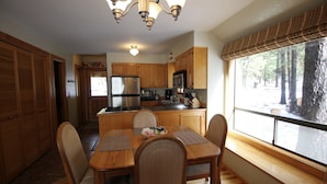 A kitchen with wooden cabinets, a refrigerator, a microwave, and a dining table with chairs. - Charming Cabin Near Fort Rock Park and SHARC! Hot Tub! 8 SHARC passes included! (Bend)
