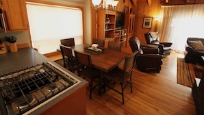 A wooden interior with a dining table, chairs, a fireplace, and a television. - Charming Cabin Near Fort Rock Park and SHARC! Hot Tub! 8 SHARC passes included! (Bend)