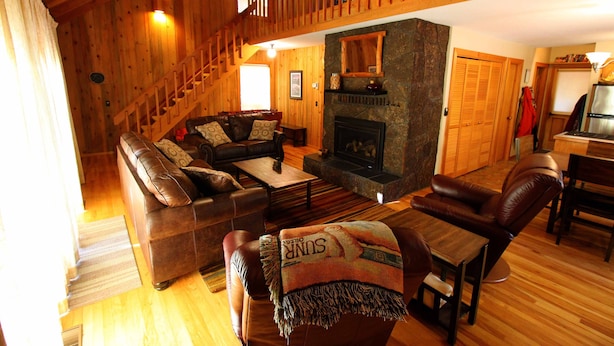 A cozy living room with a fireplace, wooden floors, a sofa set, and a dining area. - Charming Cabin Near Fort Rock Park and SHARC! Hot Tub! 8 SHARC passes included! (Bend)